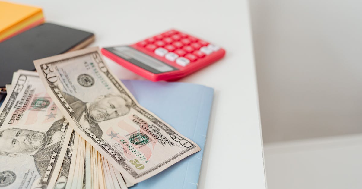 Close-up of notebooks, US dollars, and a calculator on a desk.