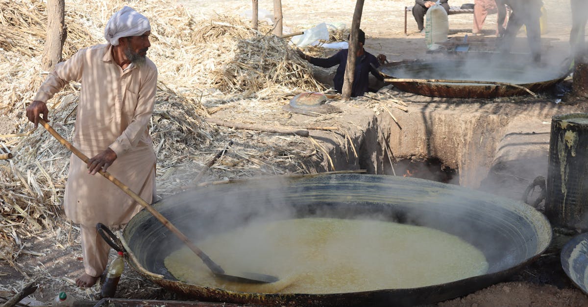 Rural workers processing sugarcane juice in traditional large pots outdoors.