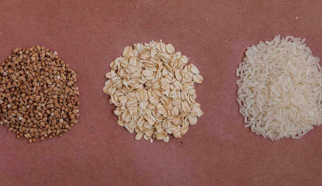 A variety of healthy grains including buckwheat, oats, and rice arranged on a flat surface.