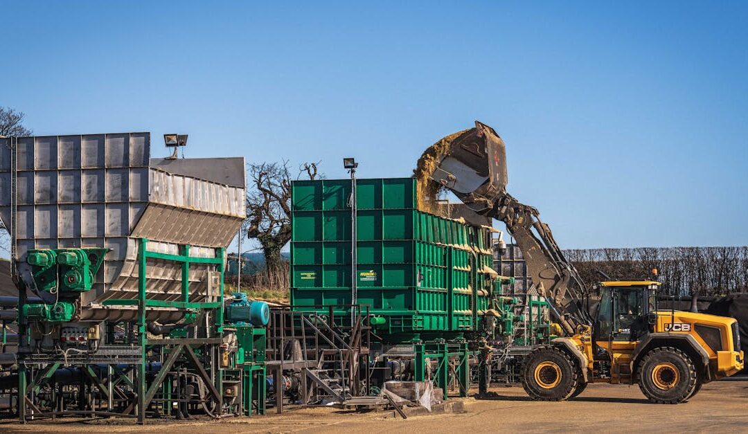 Yellow loader operating at a construction site with large green machinery under a clear blue sky.