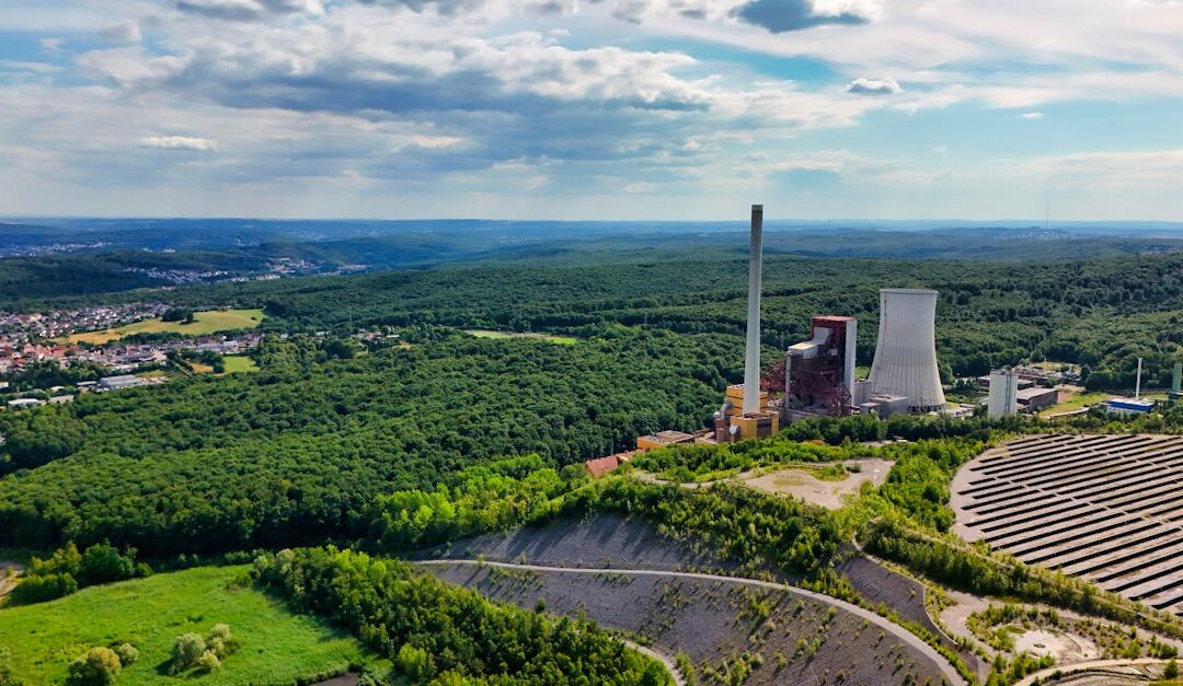 Aerial view of power plant surrounded by forests and clear skies, capturing nature-industry contrast.
