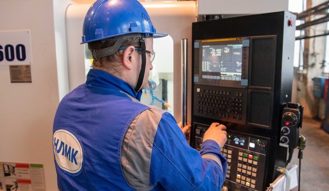 Russian factory worker in blue uniform operating CNC machine indoors.
