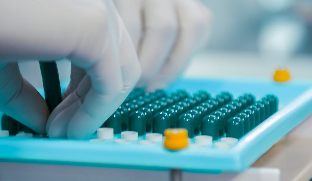 Close-up of gloved hands working with capsules in a pharmaceutical lab setting.