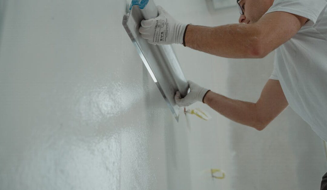 A man works on home renovation, applying plaster to an interior wall for a smooth finish.