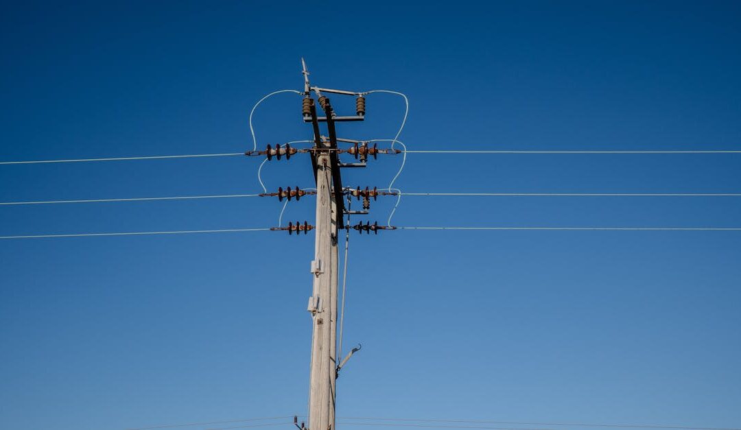 A tall wooden electric utility pole with wires against a cloudless blue sky.