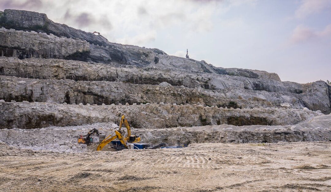 A quarry with excavators working on rocky terrain under a cloudy sky.
