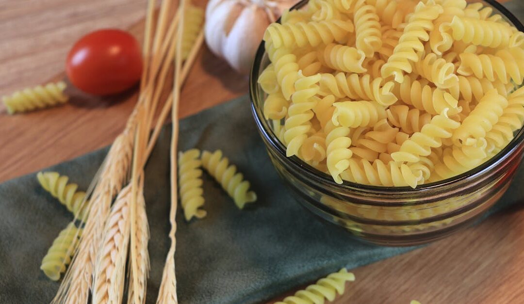 Close-up of spiral pasta, wheat, and garlic on a rustic table setting, perfect for recipe illustrations.