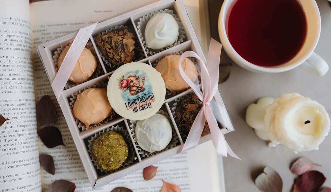 Box of assorted sweets and tea cup on a cozy setup with open book.