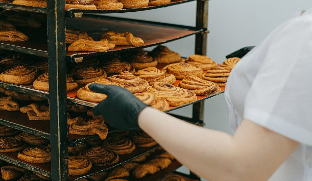 Baker placing freshly baked cinnamon rolls on a cooling rack in a bakery kitchen.
