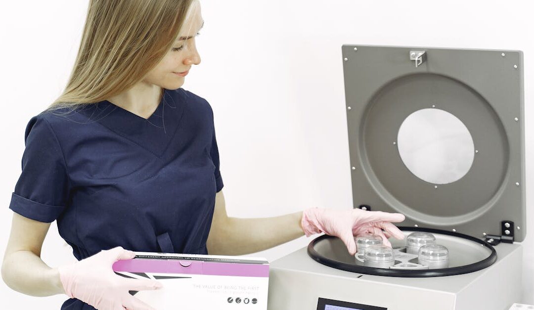 A healthcare worker using a centrifuge in a clinical setting, wearing gloves and scrub suit.