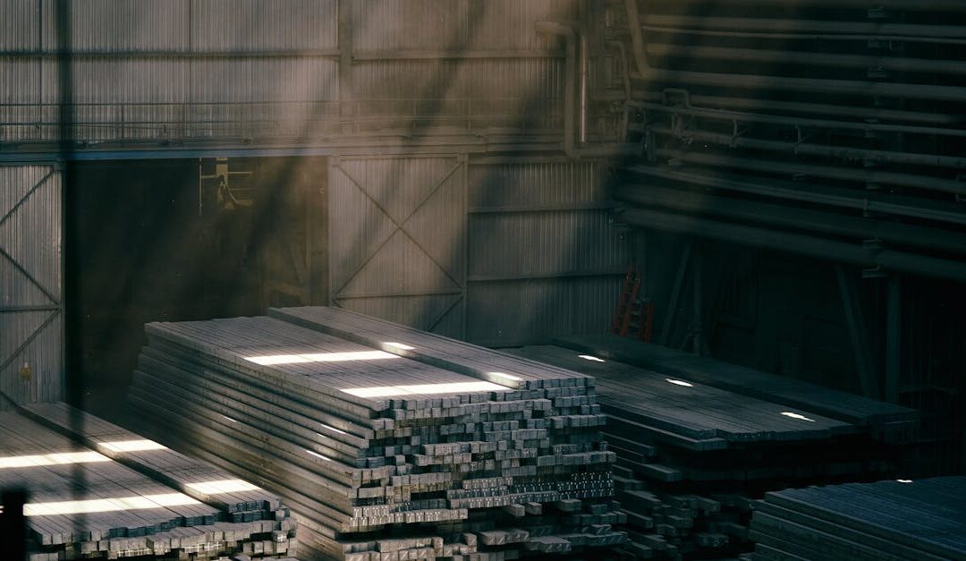 Sunlight streams into an industrial warehouse illuminating stacked steel beams.