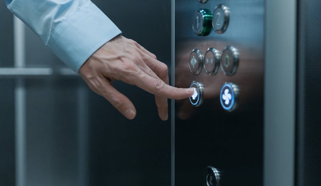 A person pressing an elevator button in a modern building, highlighting technology and urban life.