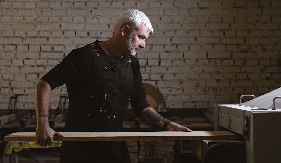 Concentrated experienced artisan in uniform processing timber board in lathe with brick walls