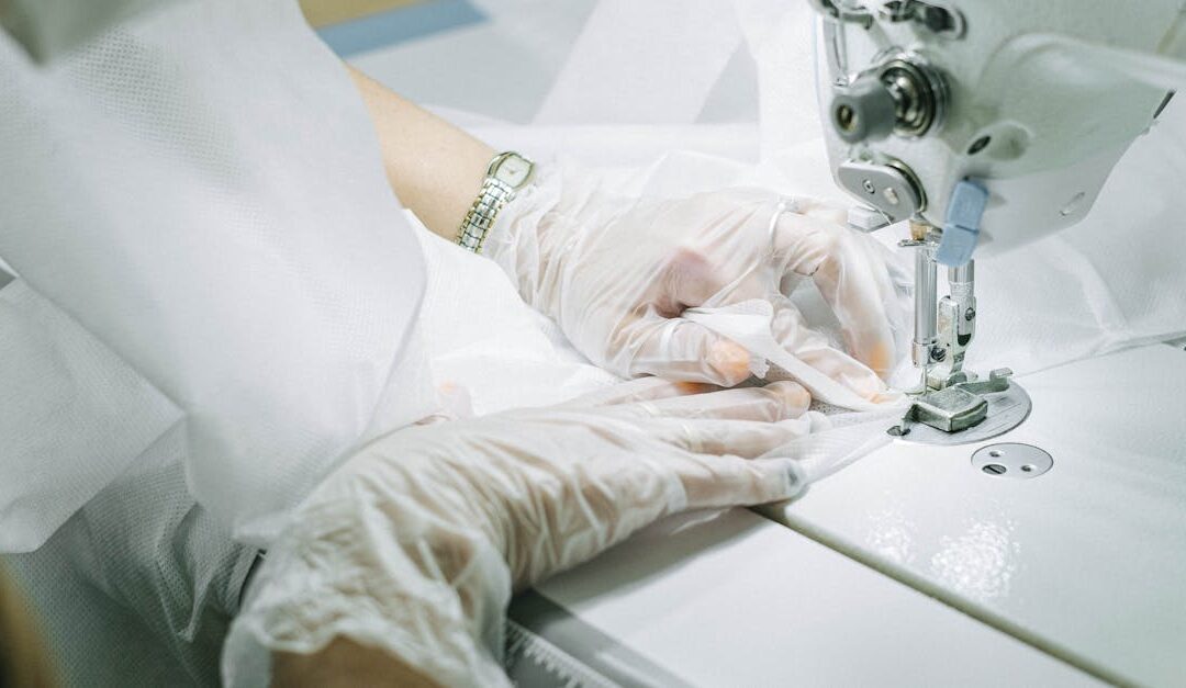 Hands in gloves working on a sewing machine, creating a garment.