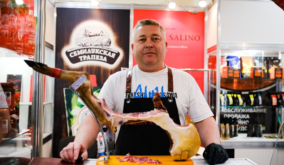 A butcher showcasing cured meat at an indoor trade show, promoting gourmet food products.