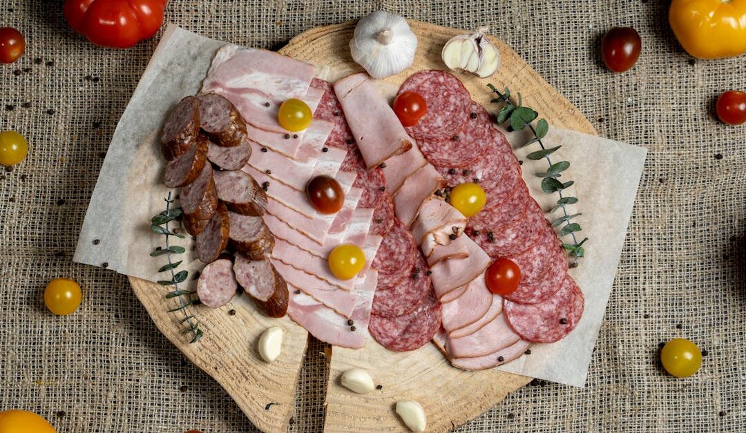 A high-angle view of assorted cured meats and fresh tomatoes on a rustic wooden board.