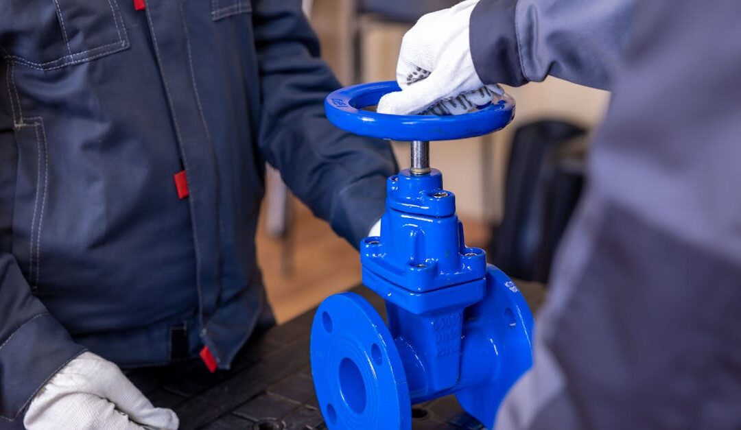 Close-up of two technicians adjusting a blue industrial valve indoors.