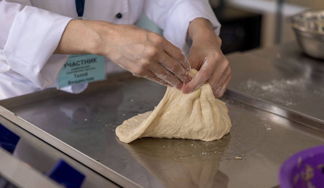 A chef skillfully kneads dough on a metal surface in a modern culinary setting.