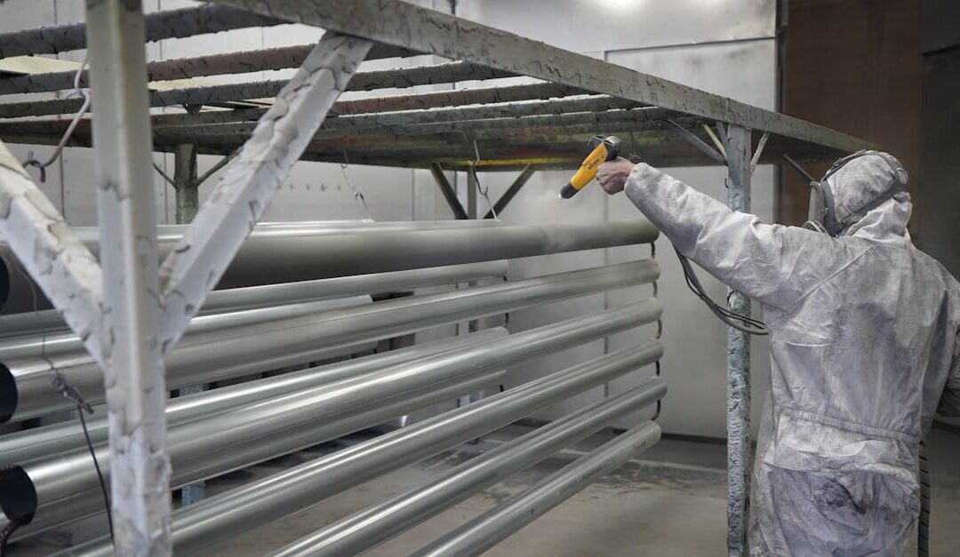 Technician applying powder coating to metal pipes in a workshop setting.
