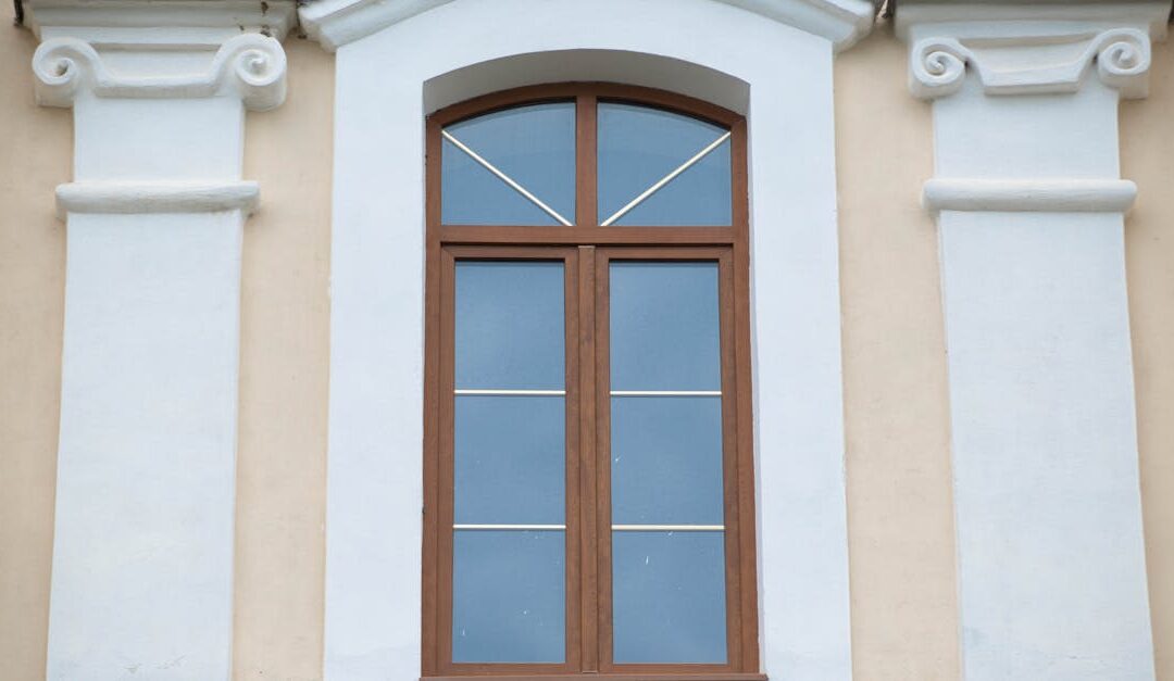 Elegant classical window surrounded by ornamental white columns and arch details on a facade.