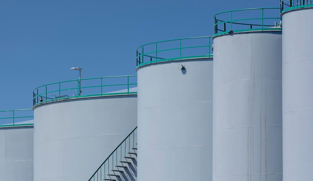 Large industrial storage tanks with green railings against a clear blue sky.