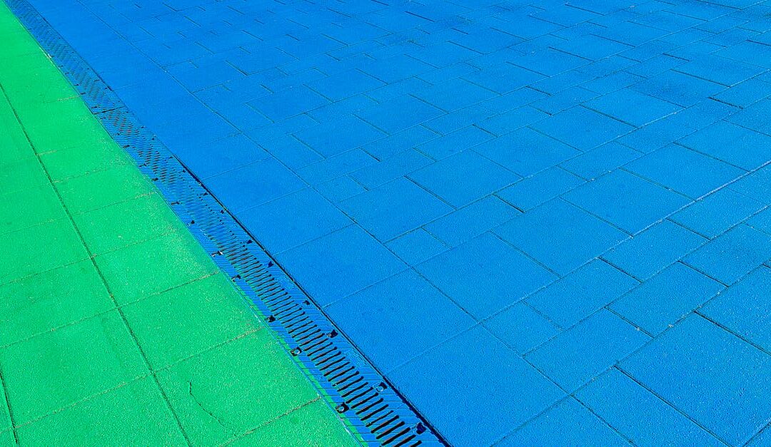 Vibrant green and blue pavement design with a drainage detail, captured outdoors.