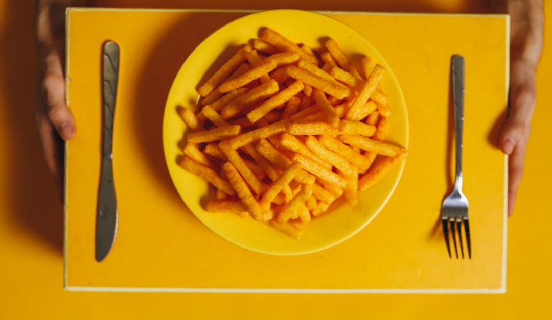 Top view of golden french fries on a plate with cutlery over a yellow background.