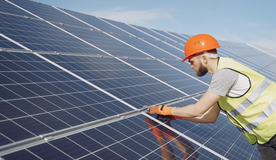 Side view of focused young man in uniform and hardhat checking setup of solar panels