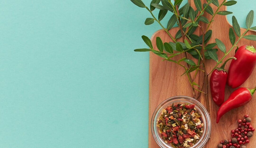 Top view of peppers, spices, and green leaves on a wooden board with teal background, offering copy space.