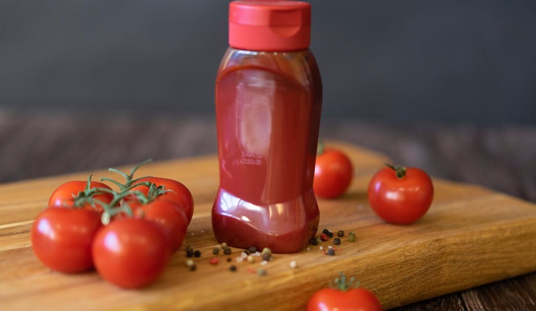 Close-up of tomatoes and ketchup bottle on a wooden board with peppercorns.