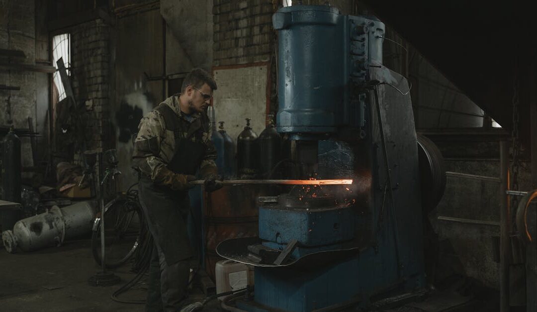 A blacksmith efficiently works with hot metal using industrial machinery in a dimly lit workshop.