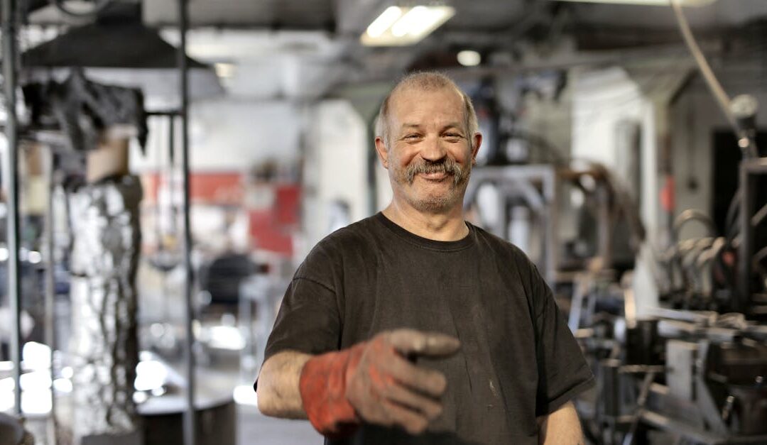 Cheerful senior white hair craftsman in heavy duty gloves laughing in workshop while looking at camera