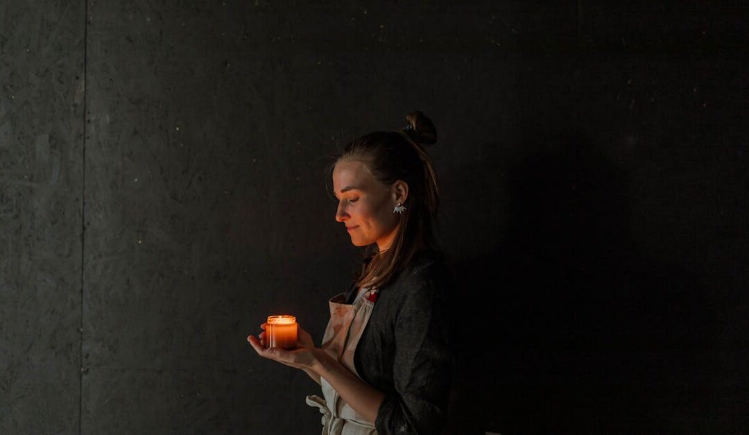 A woman in an apron holds a lit candle in a dimly lit room, creating a serene ambiance.