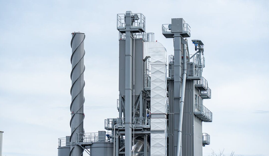 Gray industrial chimneys rise above factory buildings against a clear sky, showcasing modern industry.