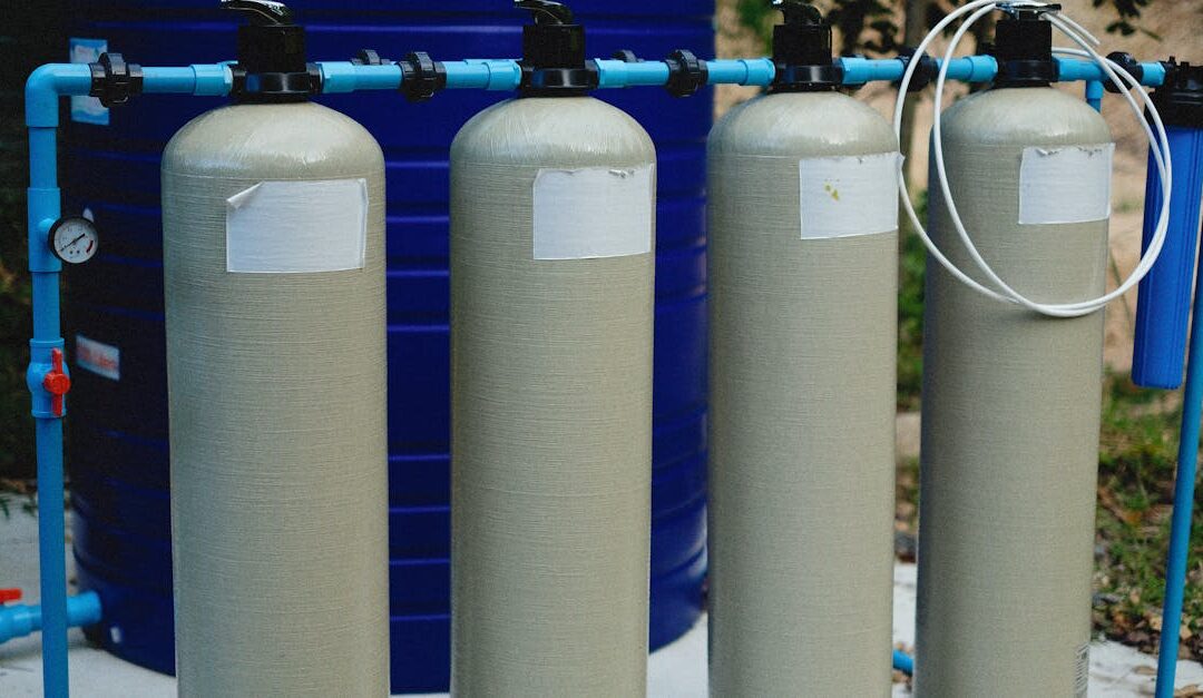 Four beige tanks in an outdoor water treatment setup with blue piping.
